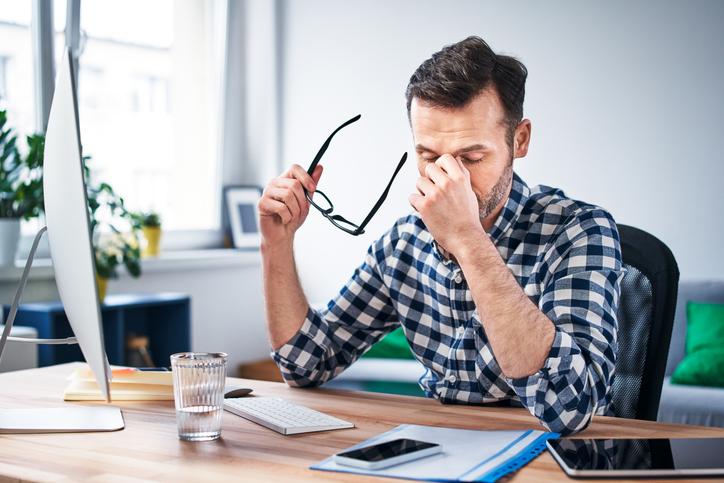 man zit achter bureau en is vermoeid